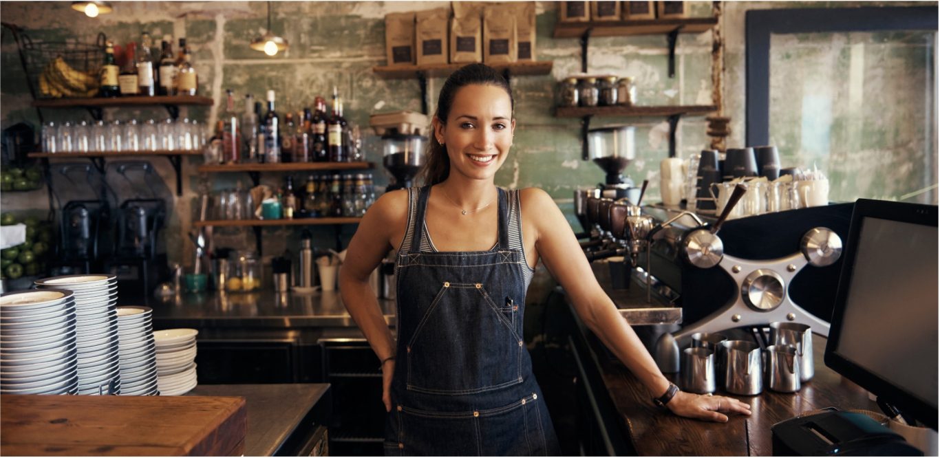 Kaffee Lächelnde Barista in einem Café mit einer Theke voller Getränke und Kaffeetassen.