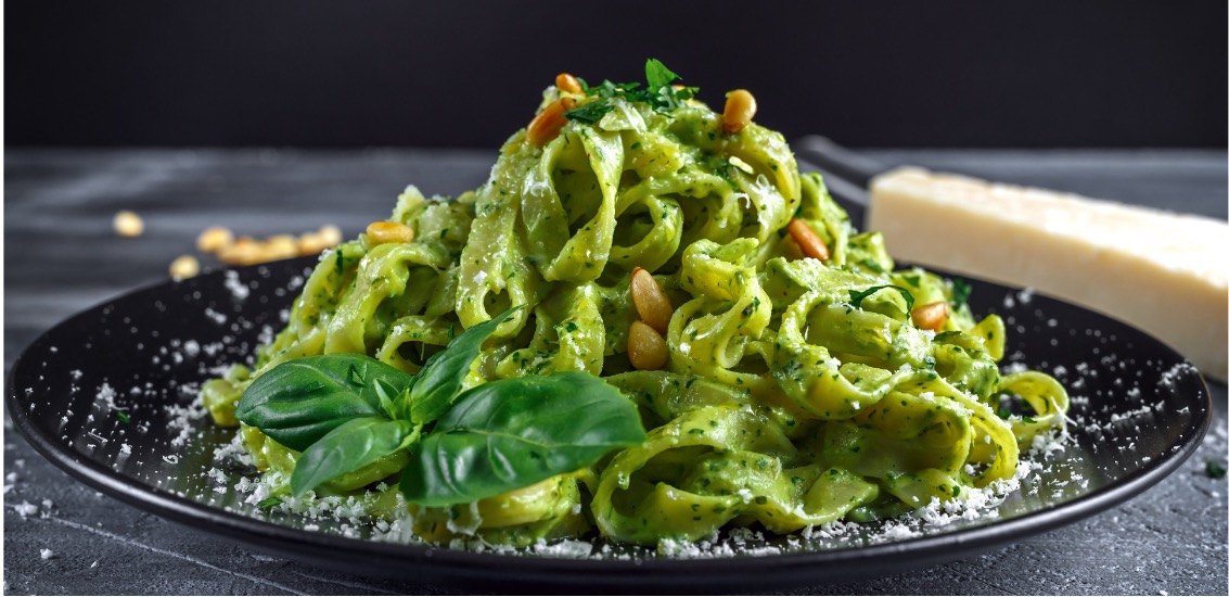 Bandnudeln mit Pesto Grüne Fettuccine mit Pesto, Pinienkernen und frischem Basilikum auf schwarzem Teller.