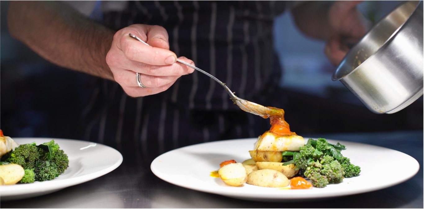 Teller anrichten Ein Koch platziert mit einer Löffel Soße auf einem Teller mit Gemüse und Kartoffeln.