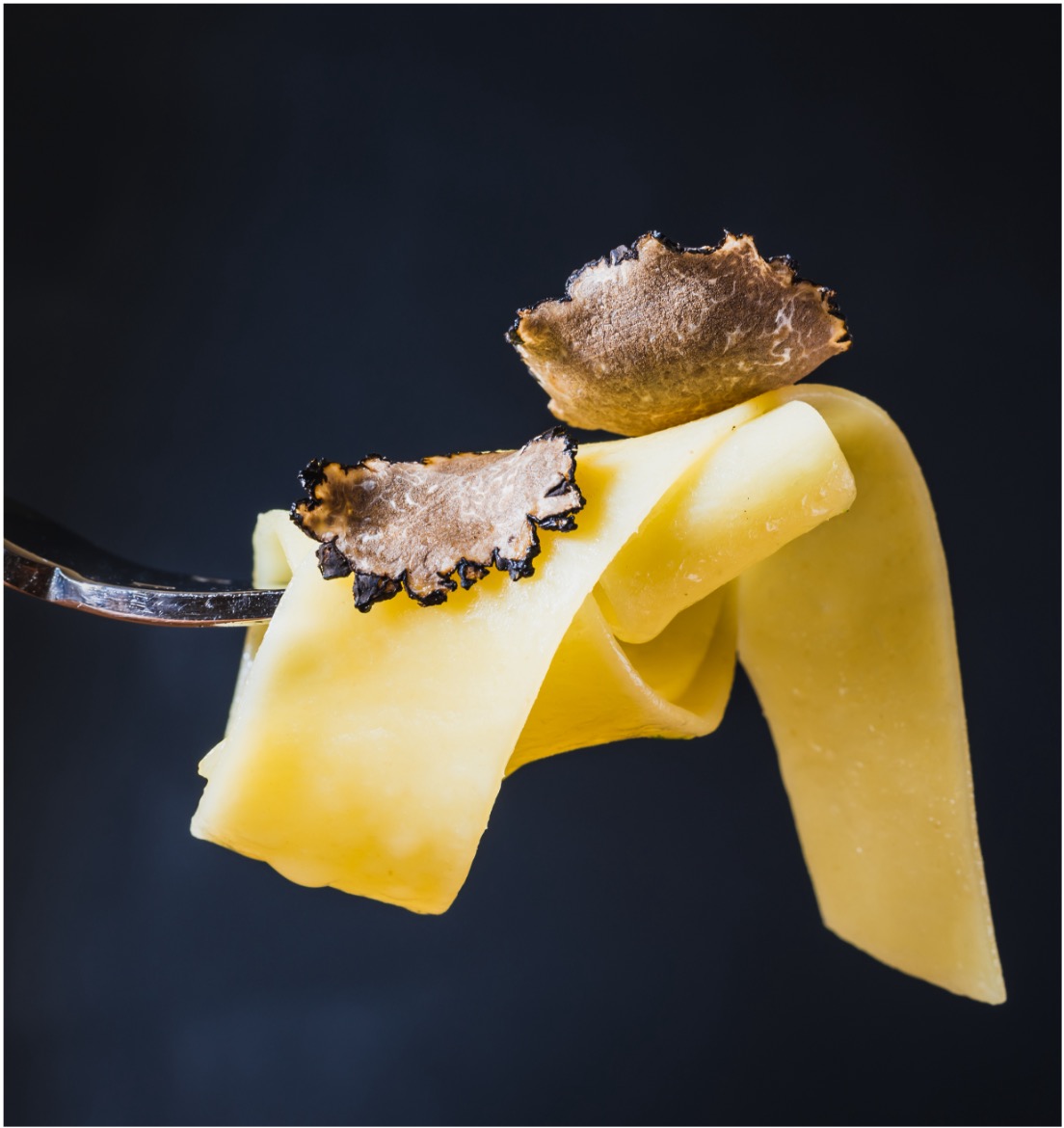 Pasta mit Trüffel Eine Gabel mit Bandnudeln, garniert mit schwarzen Trüffelscheiben.
